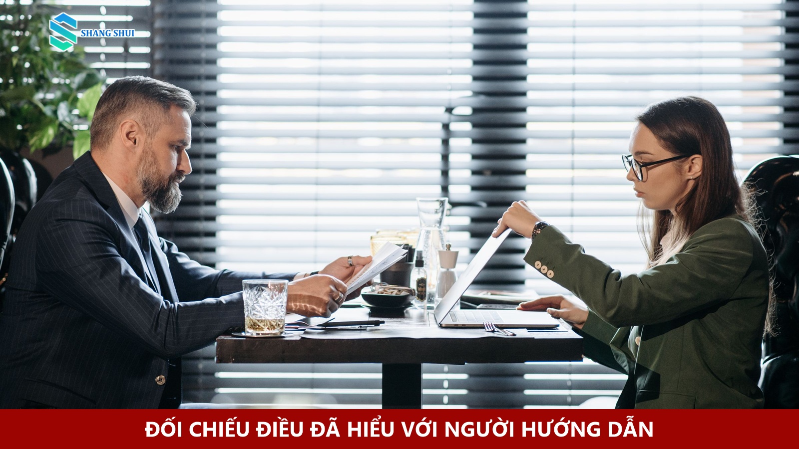 Hai người xem tài liệu và máy tính xách tay tại bàn.