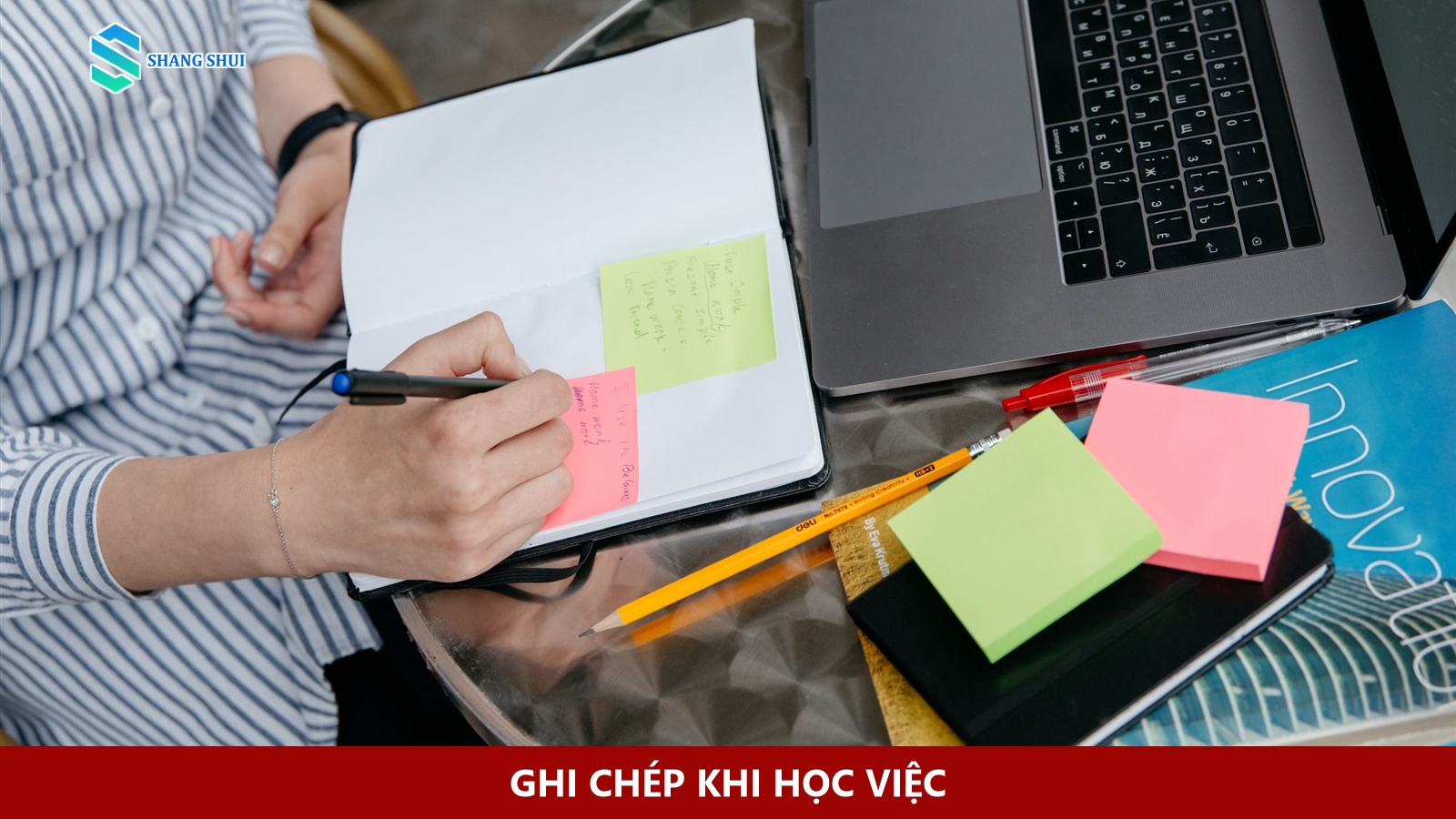 Một người viết lên giấy ghi chú đặt trong sổ bên cạnh laptop.